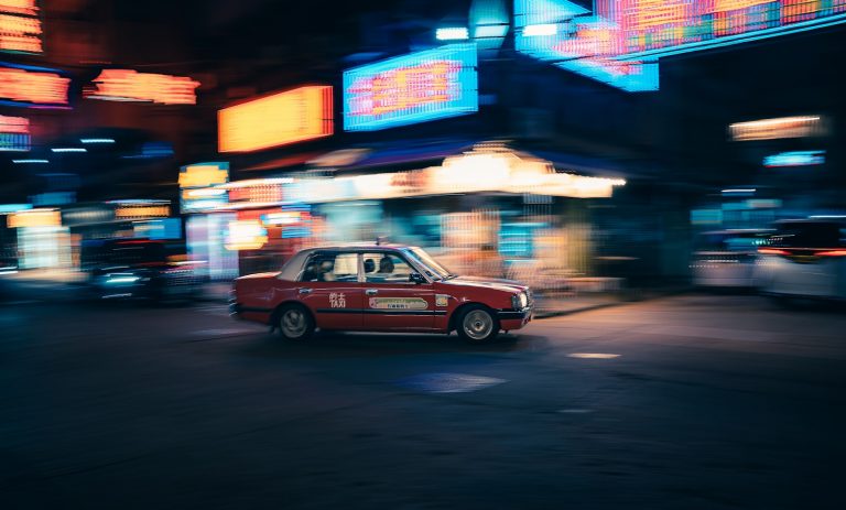 Red taxi driving through a blurry neon city at night
