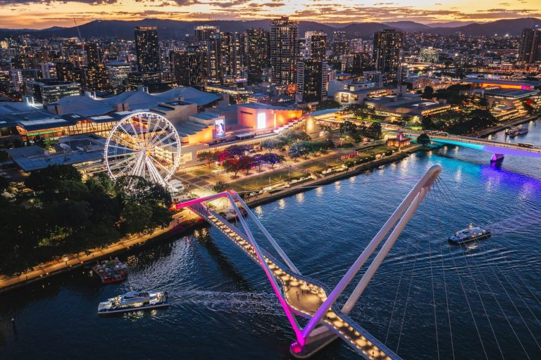 Aerial view of the illuminated Brisbane River, Kurilpa Bridge, and city skyline at night